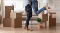 Close up young husband in jeans lift wife surrounded by cardboard boxes excited to move in new flat, happy african American couple have fun hug feel euphoric relocating together to own house