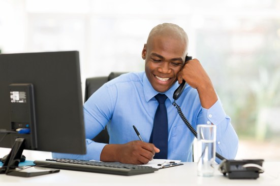 happy african businessman talking on landline phone and writing report