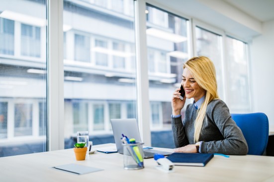 Young happy businessman reading an e-mail on laptop while communicating over smart phone in the office.