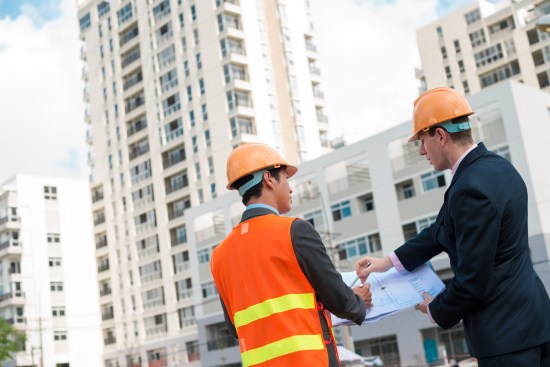 Architect and client discussing the plan of the building at the construction site, rear view