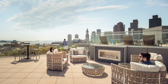 The landscaped rooftop has distinct levels for a pool and fireplace seating, a curved glass railing to keep views unobstructed, and mounds with grasses to offer a sense of a room and help withstand wind and cold.