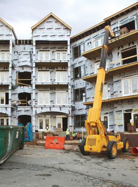 A crane lifts supplies to workers on the top floor through an opening in the weatherproofing-covered exterior.
