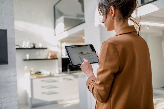 Woman controlling smart home devices using a digital tablet with launched application in the white living room. Smart home concept Processed with VSCO with c6 preset