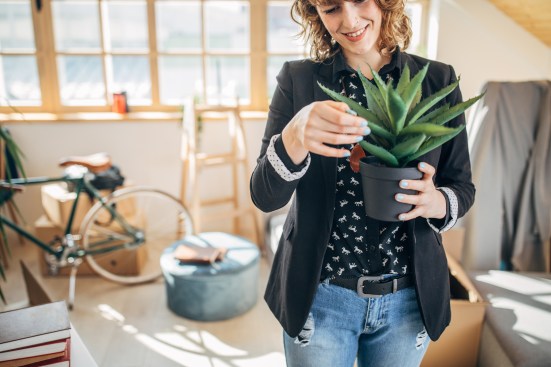 One woman, young lady moved into her new apartment, holding a plant.
